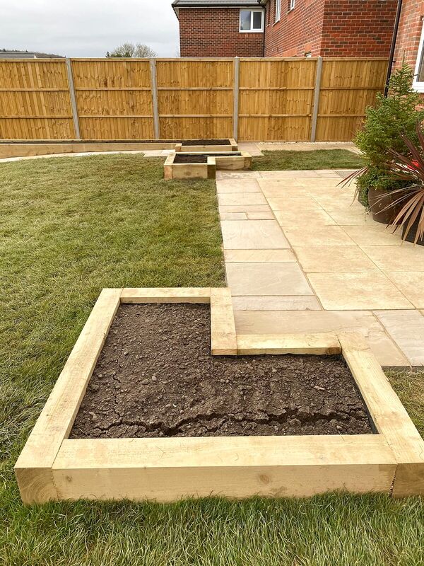 Sandstone patio and path with timber sleeper raised beds set into a lawn